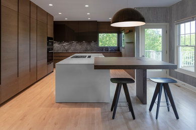Photo of a large contemporary l-shaped open plan kitchen in Other with an undermount sink, flat-panel cabinets, medium wood cabinets, quartzite benchtops, grey splashback, marble splashback, panelled appliances, light hardwood floors, with island and white benchtop.