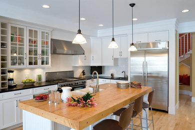 Example of a beach style l-shaped kitchen design in Other with a farmhouse sink, glass-front cabinets, white cabinets, granite countertops, white backsplash, porcelain backsplash and stainless steel appliances