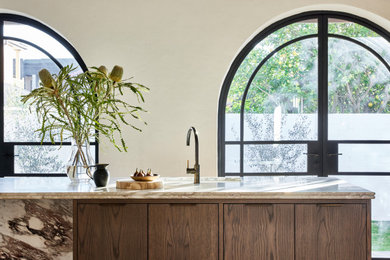 Large transitional galley eat-in kitchen in Sydney with a single-bowl sink, flat-panel cabinets, dark wood cabinets, marble benchtops, multi-coloured splashback, marble splashback, black appliances, light hardwood floors, with island, brown floor, multi-coloured benchtop and exposed beam.