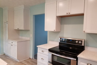 Example of a mid-sized beach style l-shaped porcelain tile and brown floor eat-in kitchen design in Jacksonville with a farmhouse sink, shaker cabinets, white cabinets, quartz countertops, stainless steel appliances, a peninsula and white countertops