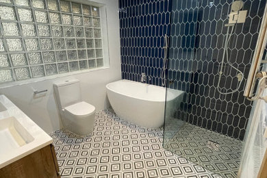 Mid-sized modern master bathroom in Melbourne with brown cabinets, a freestanding tub, a corner shower, a two-piece toilet, blue tile, ceramic tile, white walls, cement tiles, an undermount sink, engineered quartz benchtops, white floor, a hinged shower door, white benchtops, a niche, a double vanity and a floating vanity.