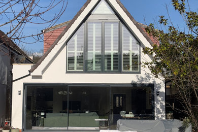 This is an example of a large and white modern two floor rear house exterior in London with a pitched roof and a red roof.