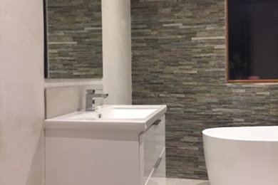 Medium sized contemporary family bathroom in Dublin with freestanding cabinets, white cabinets, a freestanding bath, a one-piece toilet, grey tiles, porcelain tiles, grey walls, porcelain flooring and a wall-mounted sink.
