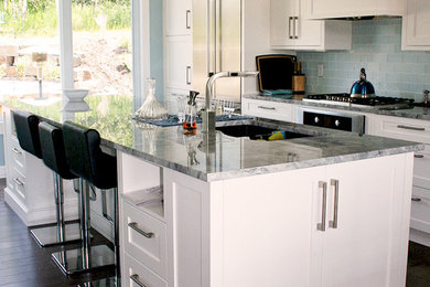 Inspiration for a mid-sized transitional l-shaped light wood floor and brown floor enclosed kitchen remodel in Calgary with an undermount sink, shaker cabinets, white cabinets, granite countertops, blue backsplash, glass tile backsplash, stainless steel appliances and an island