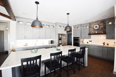 Example of a large farmhouse l-shaped dark wood floor and brown floor kitchen design in Other with a farmhouse sink, shaker cabinets, gray cabinets, quartzite countertops, white backsplash, subway tile backsplash, stainless steel appliances, an island and white countertops