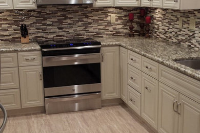 Kitchen - large traditional l-shaped light wood floor kitchen idea in Minneapolis with a double-bowl sink, raised-panel cabinets, white cabinets, granite countertops, multicolored backsplash, matchstick tile backsplash, stainless steel appliances and an island