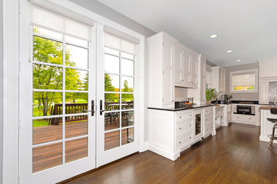 Elegant medium tone wood floor kitchen photo in New York with recessed-panel cabinets, white cabinets, quartzite countertops, white backsplash, stone slab backsplash and an island