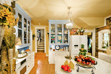 Example of a mid-sized classic light wood floor eat-in kitchen design in Kansas City with glass-front cabinets, an island, a drop-in sink, white cabinets, blue backsplash and stainless steel appliances