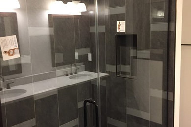 Mid-sized arts and crafts master porcelain tile medium tone wood floor and brown floor alcove shower photo in Cedar Rapids with beige walls, a hinged shower door, recessed-panel cabinets, dark wood cabinets, an undermount sink, solid surface countertops and white countertops