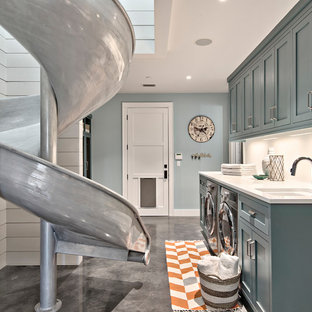 オースティンの大きいカントリー風おしゃれな洗濯室 (アンダーカウンターシンク、シェーカースタイル扉のキャビネット、コンクリートの床、左右配置の洗濯機・乾燥機、青いキャビネット、大理石カウンター、青い壁、グレーの床、白いキッチンカウンター) の写真