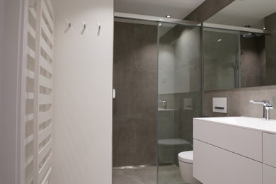 Geräumiges Modernes Duschbad mit flächenbündigen Schrankfronten, weißen Schränken, Duschnische, Wandtoilette, grauen Fliesen, weißer Wandfarbe, integriertem Waschbecken, Mineralwerkstoff-Waschtisch, grauem Boden, Schiebetür-Duschabtrennung, weißer Waschtischplatte, Einzelwaschbecken und schwebendem Waschtisch in München