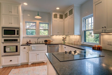 Example of a mid-sized country u-shaped medium tone wood floor and brown floor kitchen design in Omaha with a farmhouse sink, shaker cabinets, white cabinets, white backsplash, subway tile backsplash, stainless steel appliances, a peninsula and granite countertops