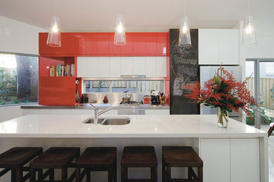 This is an example of a contemporary galley kitchen in Sydney with a double-bowl sink, flat-panel cabinets, red cabinets and white appliances.
