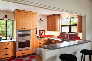 Example of a small trendy galley multicolored floor enclosed kitchen design in Portland with an integrated sink, flat-panel cabinets, medium tone wood cabinets, quartz countertops, red backsplash, ceramic backsplash, stainless steel appliances, no island and black countertops