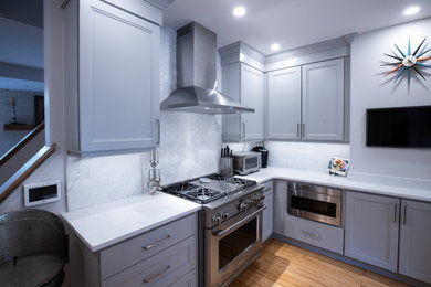 This is an example of a small transitional l-shaped separate kitchen in Philadelphia with an undermount sink, recessed-panel cabinets, quartz benchtops, stainless steel appliances, medium hardwood floors and white benchtop.