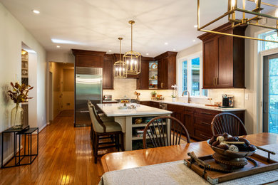 Foto på ett stort vintage vit kök, med en undermonterad diskho, luckor med infälld panel, skåp i mörkt trä, bänkskiva i kvarts, vitt stänkskydd, stänkskydd i keramik, rostfria vitvaror, mellanmörkt trägolv, en köksö och brunt golv