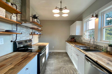 Example of a farmhouse galley vinyl floor and gray floor eat-in kitchen design in Other with a drop-in sink, shaker cabinets, white cabinets, wood countertops, gray backsplash, glass tile backsplash, stainless steel appliances, no island and brown countertops