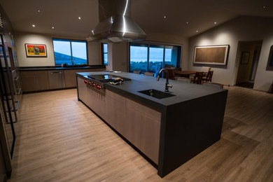 Example of a large minimalist u-shaped eat-in kitchen design in Hawaii with an integrated sink, flat-panel cabinets, light wood cabinets, black backsplash, stone slab backsplash, stainless steel appliances, an island and black countertops