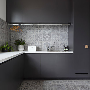 メルボルンの中サイズのコンテンポラリースタイルのおしゃれな家事室 (磁器タイルの床、アンダーカウンターシンク、フラットパネル扉のキャビネット、黒いキャビネット、グレーの床、白い壁) の写真