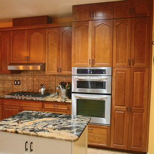 Aménagement d'une arrière-cuisine sud-ouest américain en L de taille moyenne avec un sol en travertin, un placard avec porte à panneau surélevé, des portes de placard en bois brun, une crédence en carreau de verre, un électroménager en acier inoxydable, un îlot central, un sol beige, un plan de travail en granite et une crédence marron.