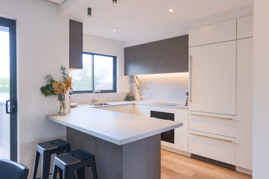 Inspiration for a mid-sized contemporary u-shaped open plan kitchen in Sydney with a drop-in sink, grey cabinets, grey splashback, stainless steel appliances, medium hardwood floors, with island and grey benchtop.