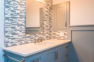Example of a mid-sized transitional 3/4 white tile and marble tile gray floor alcove shower design in Burlington with shaker cabinets, beige walls, an undermount sink, gray cabinets, quartz countertops, a hinged shower door and beige countertops