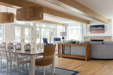 Example of a large beach style light wood floor and exposed beam great room design in Milwaukee with white walls, a standard fireplace and a stone fireplace
