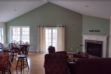 Inspiration for a large contemporary open concept light wood floor, brown floor and vaulted ceiling family room remodel in Providence with green walls, a standard fireplace, a wood fireplace surround and a wall-mounted tv