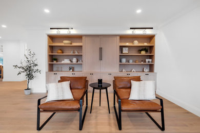 Imagen de sala de estar con biblioteca abierta grande con paredes blancas, suelo de madera clara, pared multimedia y suelo marrón