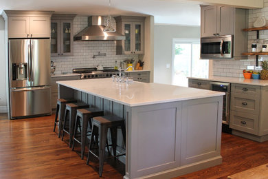 Enclosed kitchen - large transitional l-shaped dark wood floor and brown floor enclosed kitchen idea in New York with a farmhouse sink, shaker cabinets, gray cabinets, marble countertops, white backsplash, subway tile backsplash, stainless steel appliances and an island