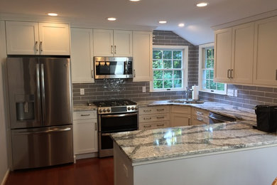 Photo of a mid-sized transitional u-shaped open plan kitchen in Baltimore with a double-bowl sink, shaker cabinets, white cabinets, quartz benchtops, grey splashback, ceramic splashback, stainless steel appliances, medium hardwood floors, no island, red floor and grey benchtop.