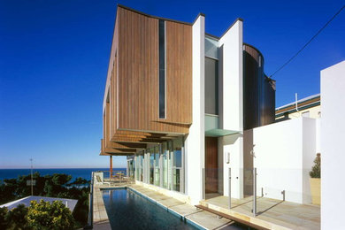 Design ideas for a contemporary two-storey white exterior in Gold Coast - Tweed with wood siding and a flat roof.