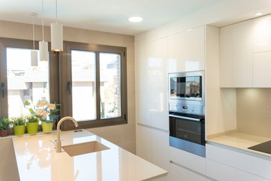 Photo of a mid-sized modern u-shaped kitchen in Madrid with flat-panel cabinets, white cabinets, beige splashback, concrete floors and a peninsula.