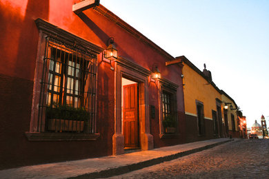 Example of a mid-sized classic red one-story stucco exterior home design in Other with a mixed material roof