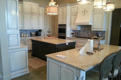 Large traditional eat-in kitchen in New Orleans with beaded inset cabinets, distressed cabinets, granite benchtops, grey splashback, mosaic tile splashback, stainless steel appliances, concrete floors and multiple islands.
