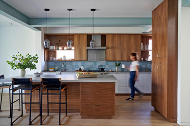 Example of a trendy galley medium tone wood floor and brown floor kitchen design in San Francisco with flat-panel cabinets, medium tone wood cabinets, blue backsplash, stainless steel appliances, an island and gray countertops