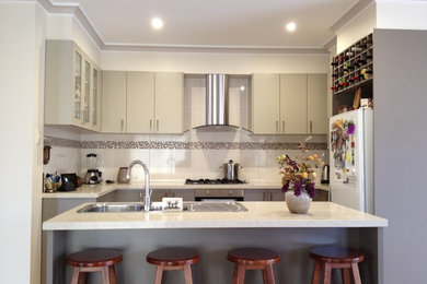 Mid-sized modern u-shaped kitchen in Melbourne with a drop-in sink, beige cabinets, quartz benchtops, white splashback, ceramic splashback, stainless steel appliances and with island.
