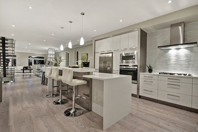 Open concept kitchen - mid-sized contemporary single-wall laminate floor and brown floor open concept kitchen idea in Ottawa with an undermount sink, flat-panel cabinets, white cabinets, solid surface countertops, gray backsplash, matchstick tile backsplash, stainless steel appliances, an island and white countertops