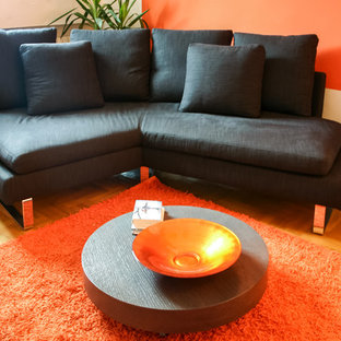 Foto di un piccolo soggiorno minimal chiuso con libreria, pareti arancioni, parete attrezzata e pavimento in legno massello medio