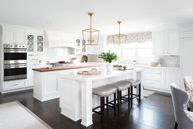 Transitional l-shaped dark wood floor and brown floor kitchen photo in New York with an undermount sink, recessed-panel cabinets, white cabinets, wood countertops, beige backsplash, two islands and brown countertops