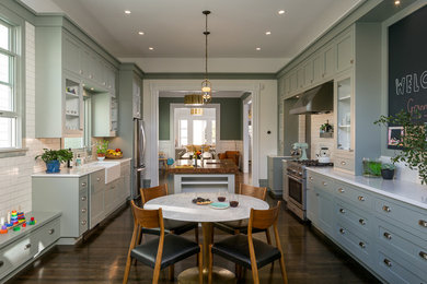 Example of an ornate dark wood floor enclosed kitchen design in San Francisco with a farmhouse sink, shaker cabinets, white backsplash, subway tile backsplash, stainless steel appliances, an island and green cabinets