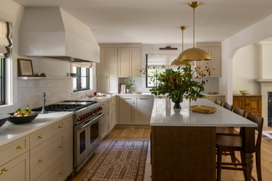 Example of a large classic l-shaped light wood floor and beige floor enclosed kitchen design in Seattle with a farmhouse sink, shaker cabinets, beige cabinets, marble countertops, white backsplash, stone slab backsplash, stainless steel appliances, white countertops and an island