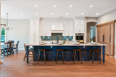 Large trendy galley vinyl floor and brown floor eat-in kitchen photo in Other with a single-bowl sink, shaker cabinets, white cabinets, quartzite countertops, blue backsplash, glass tile backsplash, stainless steel appliances, an island and white countertops