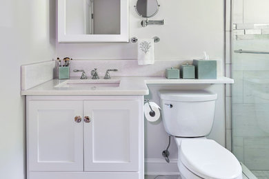 Example of a mid-sized beach style 3/4 blue tile porcelain tile and gray floor bathroom design in New York with recessed-panel cabinets, white cabinets, a one-piece toilet, blue walls, an undermount sink, quartz countertops, a hinged shower door and white countertops