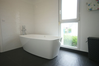 Design ideas for a medium sized contemporary ensuite bathroom in Nancy with beaded cabinets, light wood cabinets, ceramic tiles, a wall-mounted sink, an open shower, white worktops, a freestanding bath, a shower/bath combination, a two-piece toilet, white tiles, white walls, slate flooring and black floors.