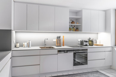Mittelgroße Moderne Küche in L-Form mit flächenbündigen Schrankfronten, weißen Schränken, Laminat-Arbeitsplatte, Küchenrückwand in Grau und grauer Arbeitsplatte
