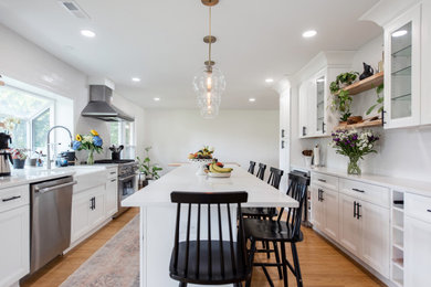 Large transitional galley porcelain tile and brown floor eat-in kitchen photo in Philadelphia with a farmhouse sink, recessed-panel cabinets, white cabinets, quartz countertops, white backsplash, subway tile backsplash, stainless steel appliances, an island and white countertops