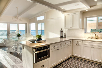 Photo of a mid-sized beach style l-shaped open plan kitchen in San Diego with an undermount sink, white cabinets, quartzite benchtops, white splashback, stainless steel appliances, louvered cabinets, stone slab splashback, medium hardwood floors, a peninsula and grey floor.