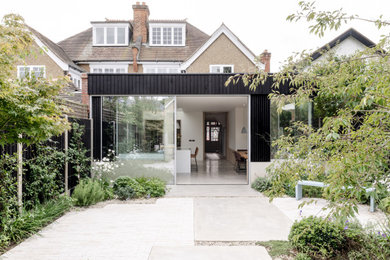 This is an example of a medium sized and black modern rear house exterior in Surrey with wood cladding, a flat roof, a green roof and board and batten cladding.