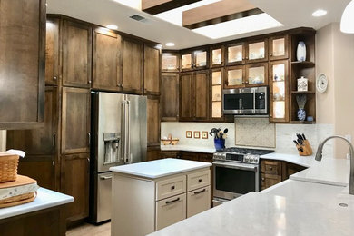 Photo of a mid-sized transitional u-shaped separate kitchen in Albuquerque with a farmhouse sink, shaker cabinets, dark wood cabinets, quartz benchtops, grey splashback, stainless steel appliances, with island and white benchtop.